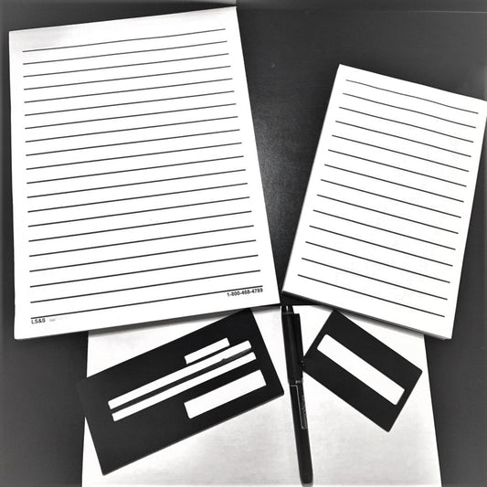 A bold line pad of paper and note pad with A checking writing guide, bravo pen, and aluminum signature guide below them