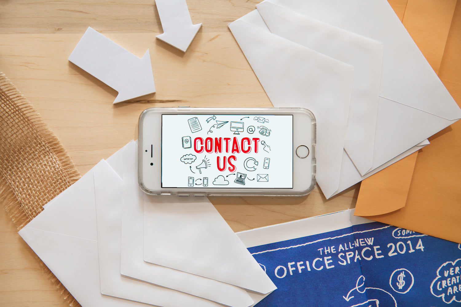 A white iPhone in the center of the image with the text across the screen saying "Contact Us". Envelopes and arrows pointing towards the phone surround it. 