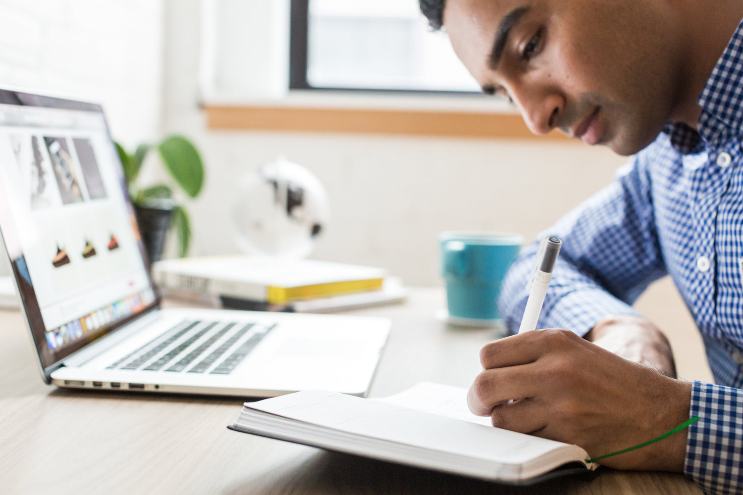 Man writing in notebook at a desk with an open computer