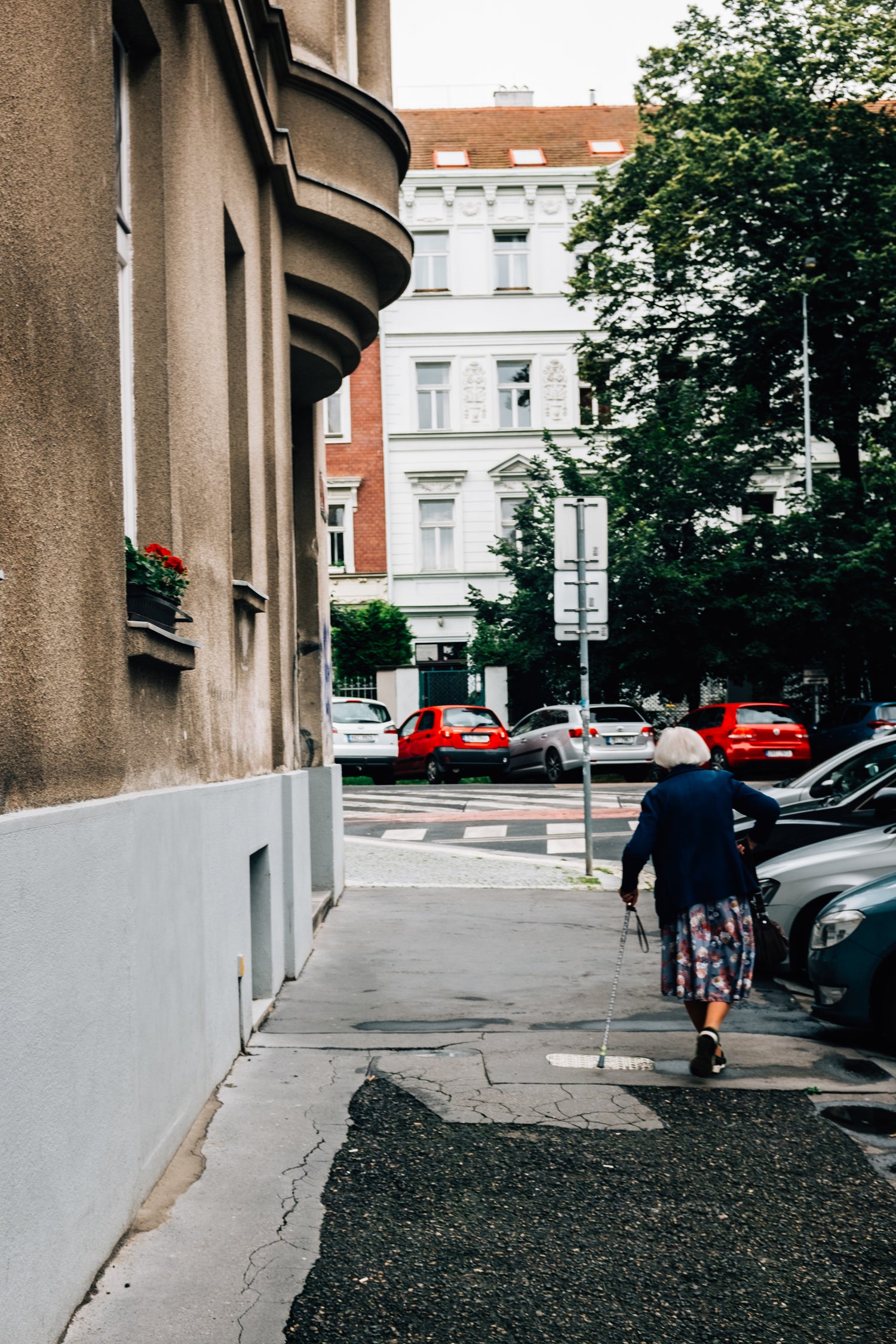Older woman walking down street towards building using a walking cane