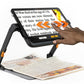 Humanware Explore 12 in it's stand showing a hand touching the touch screen while enlarging a newspaper underneath the device.