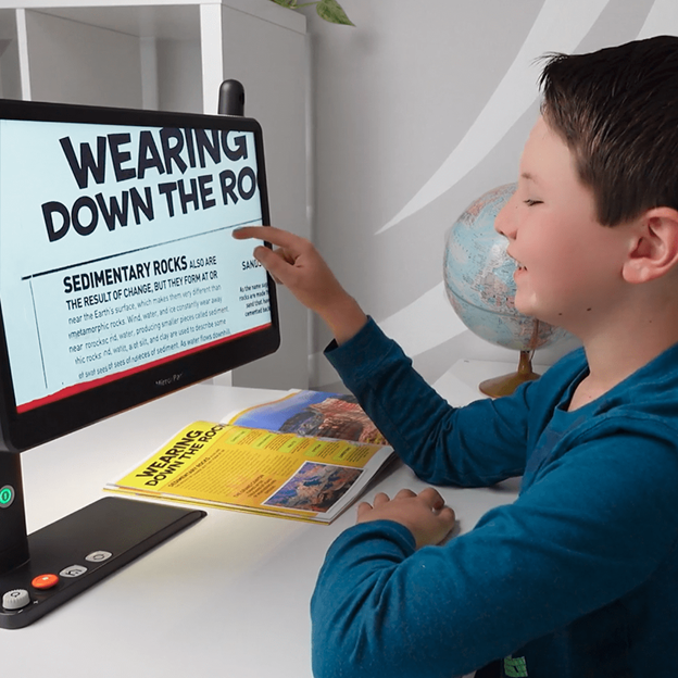 Student using MirrorPad Pro to magnify and read textbook content that is sitting on the table tap onto a large screen, supporting accessible learning and independent study.