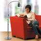 Woman sitting on a red sofa reading a large book under the light of the Flexi Vision Floor Lamp by Daylight.