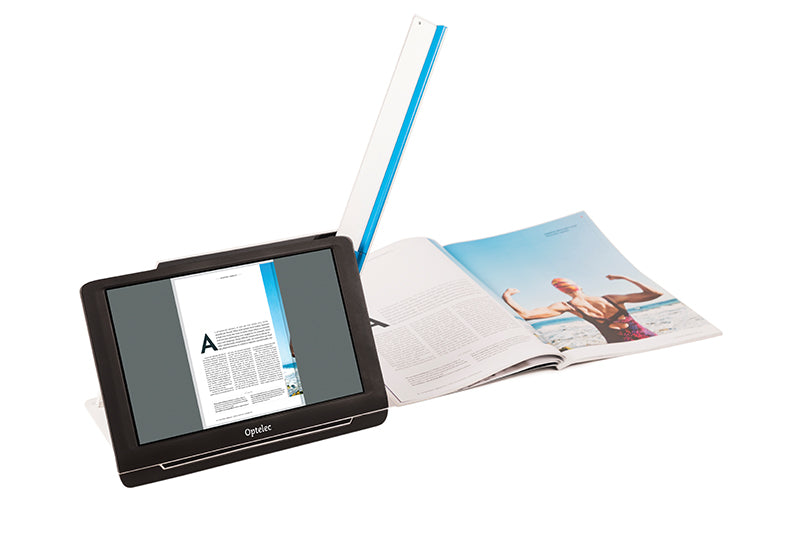 The Optelec Compact 10 With Speech is resting next to a magazine and the scanner arm of this digital magnifier is ready to scan the magazine.